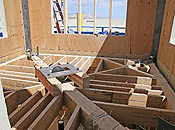 Heavy wooden joists form an interesting criss-cross pattern in the uncovered floor of a windowed plywood room.