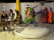 A participant tries to maintain her balance on a spinning platform as another participant pedals a stationary bike to spin her.